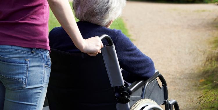 Kvinde med lilla t-shirt skubber kørestol med ældre kvinde.